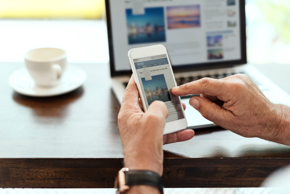 Person browsing a website on a smartphone with a laptop in the background, illustrating mobile shopping